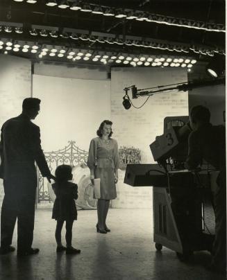 "Television broadcaster Dorothy Wootton rehearses as husband and child stand by"
